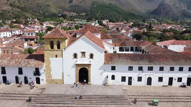 Drone shot of colonial main square in small town of Villa de Leyva, Boyaca, Colombia. Tracking video shot from left to right, showing the church, mountains, trees and greenery.
