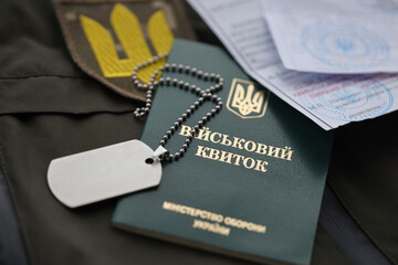 Military token or army ID ticket with mobilization notice lies on green ukrainian military uniform...