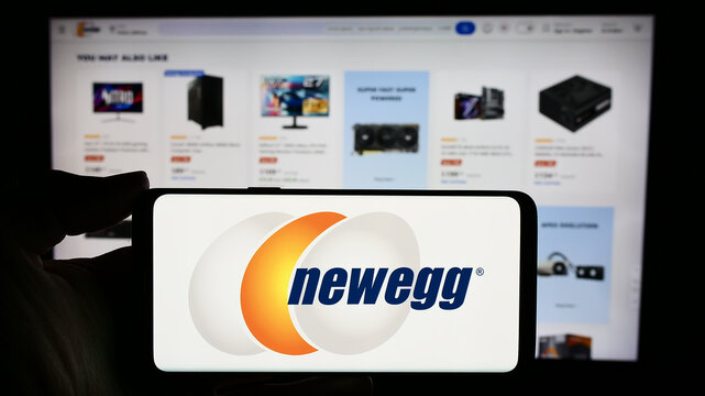 Stuttgart, Germany - 02-24-2024: Person holding cellphone with logo of US computer retail company Newegg Commerce Inc. in front of business webpage. Focus on phone display.