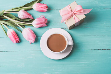 Fototapeta na wymiar Pink tulips, a cup of coffee and gift in a box on a turquoise wooden table. Spring festive background, top view, flat lay