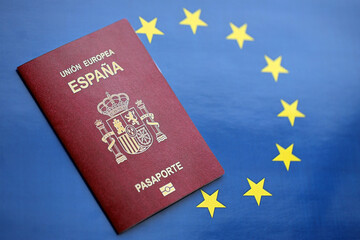 Red Spanish passport of European Union on blue flag background close up. Tourism and citizenship...