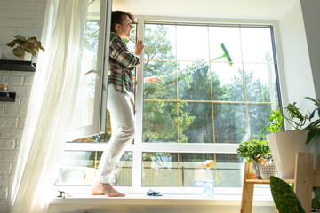Woman manually washes the window of the house with a rag with spray cleaner and mop inside the...