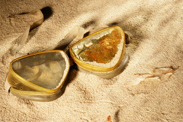 Two small, triangular, gold-colored containers are laying on the sand - 748990231