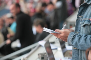 A man is writing on a piece of paper while sitting in a stadium