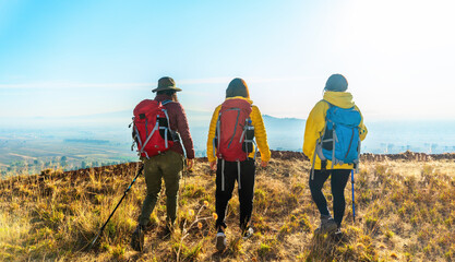 Three people walk up the mountain with hiking backpacks and yellow jackets, enjoying the sunrise...
