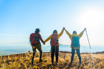 Three friends in yellow jackets and hiking backpacks reach the top of the mountain. Concept of...
