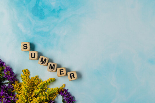 boggle cubes letters summer word on blue sky background and flowers and negative space