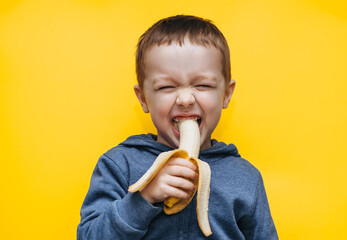 A small funny cheerful boy bites a banana, makes faces and plays around. Studio photography with...