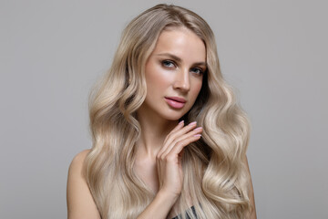 Blonde girl with long wavy hair dyeing ombre touches her hair with her hand. Beautiful fashion woman