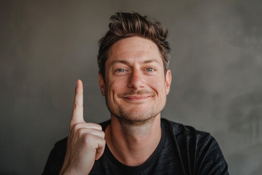 Confident man with a smirk pointing up, seeming to have an idea, against a neutral background