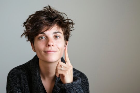 Thoughtful woman with short hair raising her finger, with a soft, neutral background