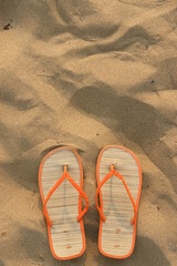 A pair of orange flip flops are on a sandy beach - 749026678