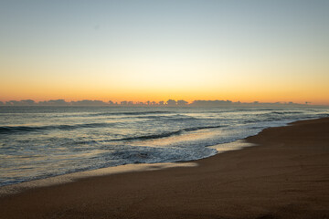 Fototapeta na wymiar Sunrise on a Florida beach, sea foam on shore, clouds above the horizon