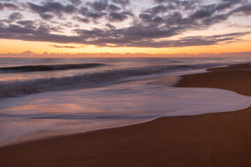 Fototapeta na wymiar Sunrise on a Florida beach, sea foam on shore, clouds above the horizon