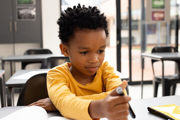 African American boy with short curly hair is focused on drawing in a school classroom