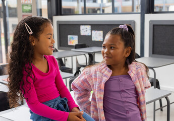 Two biracial girls are sharing a moment in a school classroom setting