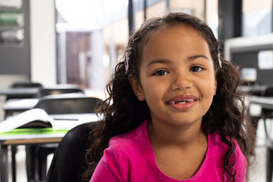Biracial girl with curly hair smiles in a school classroom setting