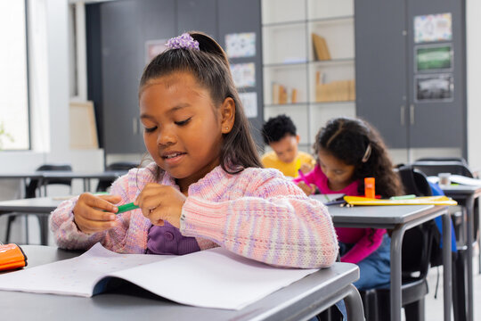 Biracial girl with a purple hair tie focuses on her schoolwork, pencil in hand