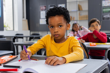 African American boy in a yellow shirt is drawing in a school classroom