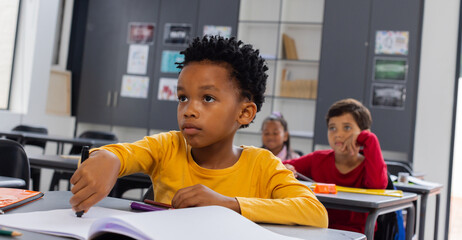 Biracial boy in a yellow shirt looks attentive in a school classroom