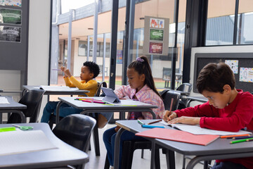 Biracial girl and boys are focused on their schoolwork in a school classroom - obrazy, fototapety, plakaty