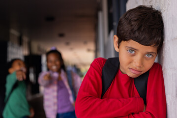 Biracial boy leans against a white wall, looking pensive, a victim of bullying in school