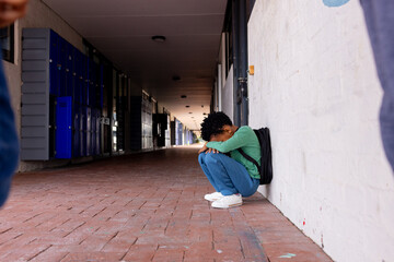 An African American boy sits alone on the ground as a bullying victim in school with copy space