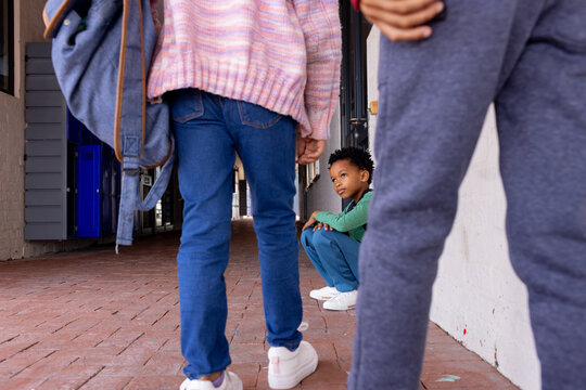 African American boy sits crouched between other children in school, looking sad