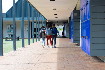 Three children walk down a school corridor, arms around each other, with copy space