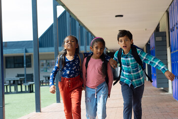 Three biracial children walk through a school corridor with lockers