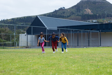 Three biracial girls are playing on a grassy field at school, with copy space