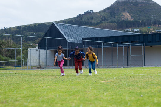 Three biracial girls are playing on a grassy field at school, with copy space