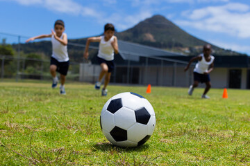 Obraz na płótnie Canvas A soccer ball in focus with three children running behind it in school