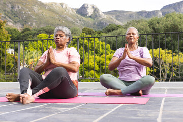 Senior African American woman and senior biracial woman are practicing yoga outdoors