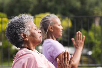 Senior African American woman and senior biracial woman practice yoga outdoors, both with grey hair