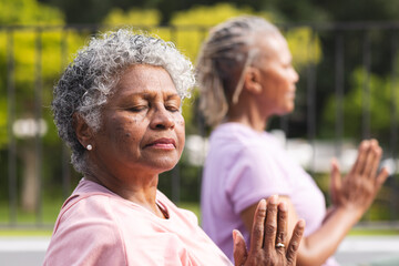 Senior African American woman and senior biracial woman practice yoga outdoors