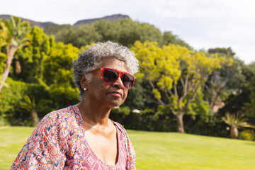Senior biracial woman with gray hair wears red sunglasses and a patterned blouse, with copy space - Powered by Adobe
