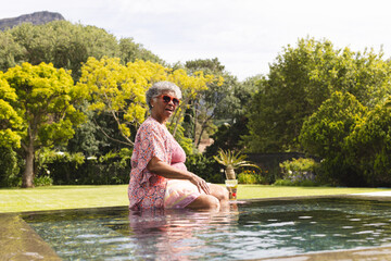 Senior biracial woman enjoys a poolside moment, her gray hair complementing the sunny day