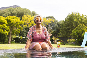 Senior biracial woman enjoys a sunny day in the pool, wearing a floral top and sunglasses