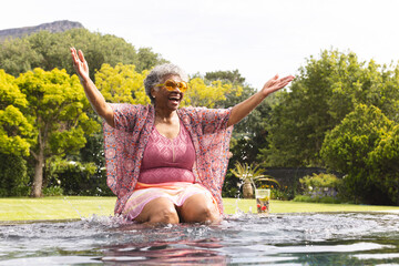 Senior biracial woman enjoys a refreshing moment in a pool, her arms spread wide with joy