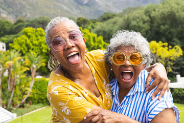 Senior African American woman and senior biracial woman share a joyful embrace outdoors