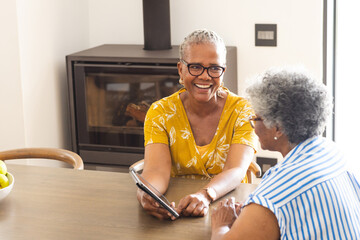 Senior biracial woman in a yellow top shares a laugh with an African American woman at home