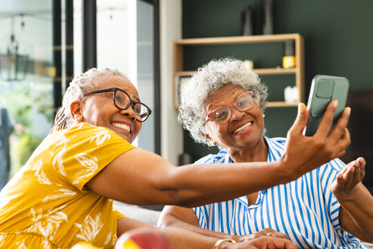 Senior African American woman and senior biracial woman are smiling while taking a selfie at home