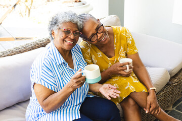 Senior African American woman and senior biracial woman share a joyful moment with coffee at home - Powered by Adobe