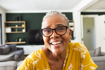 Senior African American woman smiles warmly on video call, wearing glasses and a yellow top