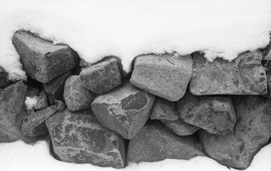 close view of stone wall covered with snow in winter in black and white