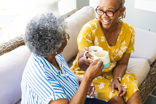 Senior African American woman and senior biracial woman share a laugh over coffee at home