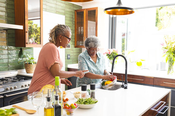 Senior African American woman and senior biracial woman are washing vegetables in a kitchen - Powered by Adobe