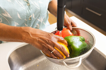 Senior biracial woman washes colorful bell peppers under a kitchen faucet - Powered by Adobe
