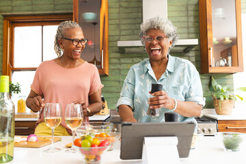 Senior African American woman and senior biracial woman share a joyful moment in a kitchen